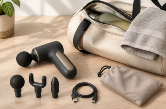 Compact massage device with three attachments, a charging cable and travel pouch beside a gym bag.