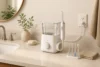 Countertop water flosser beside a bathroom sink, with a removable reservoir, pressure dial and replacement tips.